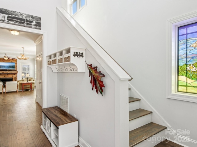 stairway with a fireplace, wood finished floors, visible vents, and a notable chandelier