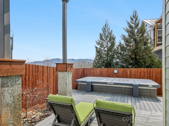 wooden deck with a fenced backyard, a mountain view, and a covered hot tub