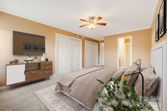 carpeted bedroom featuring visible vents, two closets, baseboards, ornamental molding, and a ceiling fan