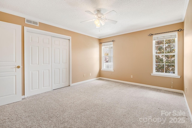 unfurnished bedroom featuring visible vents, ornamental molding, a textured ceiling, a closet, and carpet flooring