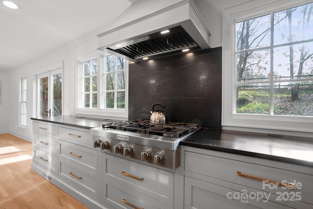 kitchen featuring custom range hood, stainless steel gas stovetop, backsplash, white cabinetry, and light wood-type flooring