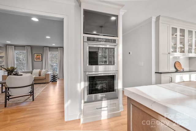 kitchen featuring stainless steel double oven, white cabinets, light wood-type flooring, glass insert cabinets, and crown molding