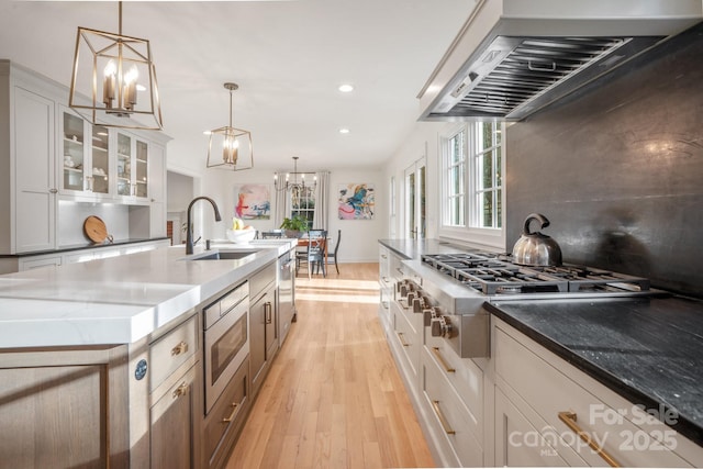 kitchen featuring stainless steel appliances, a sink, light stone countertops, wall chimney exhaust hood, and an inviting chandelier