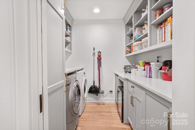 clothes washing area featuring laundry area, baseboards, ornamental molding, washing machine and clothes dryer, and light wood-type flooring