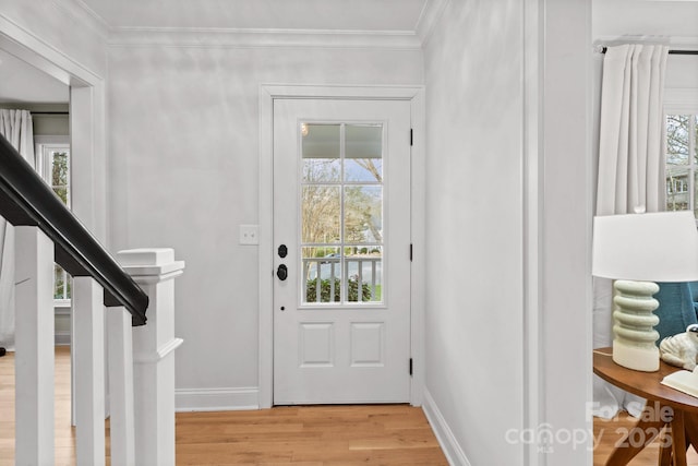 entryway with light wood finished floors, ornamental molding, and a healthy amount of sunlight