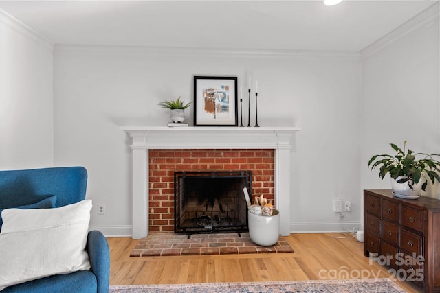 living area with ornamental molding, a brick fireplace, wood finished floors, and baseboards