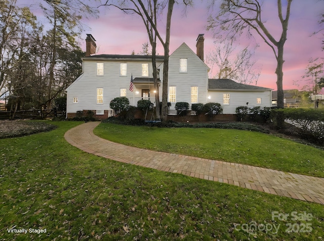 back of house at dusk with a chimney and a yard