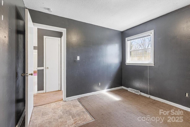 carpeted spare room featuring baseboards, visible vents, and a textured ceiling