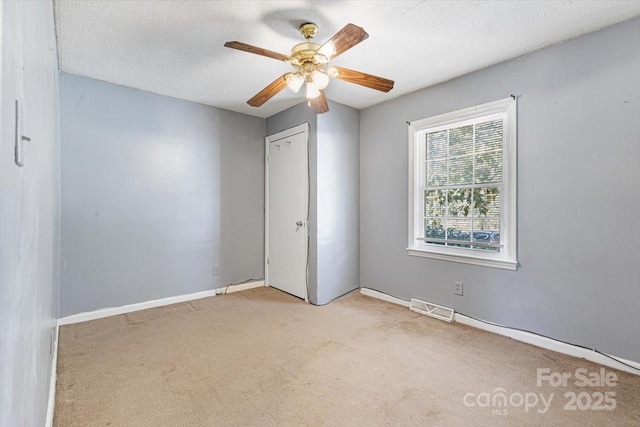 carpeted spare room with visible vents, ceiling fan, a textured ceiling, and baseboards