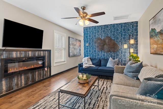 living room featuring visible vents, an accent wall, a glass covered fireplace, wood finished floors, and baseboards