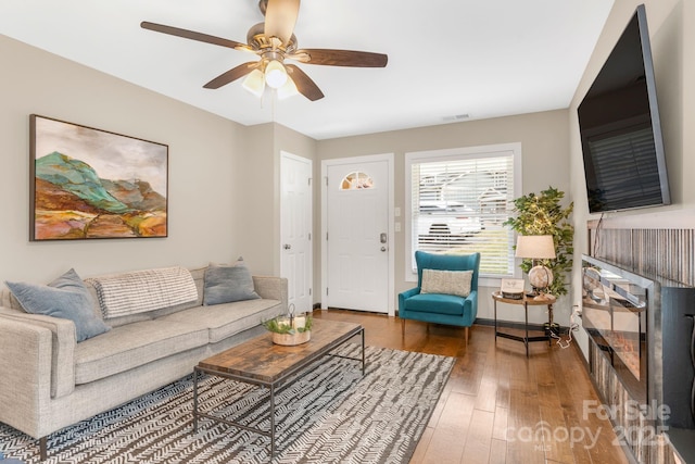 living room with a fireplace, visible vents, a ceiling fan, baseboards, and hardwood / wood-style flooring