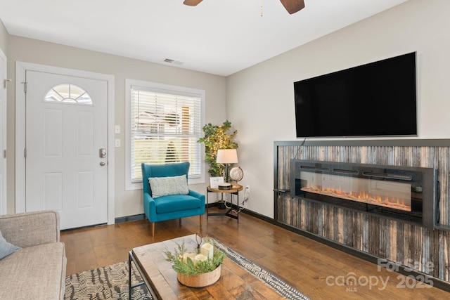 living room featuring baseboards, visible vents, wood finished floors, and a glass covered fireplace