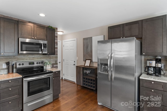 kitchen with light stone counters, dark wood-type flooring, dark brown cabinets, appliances with stainless steel finishes, and decorative backsplash