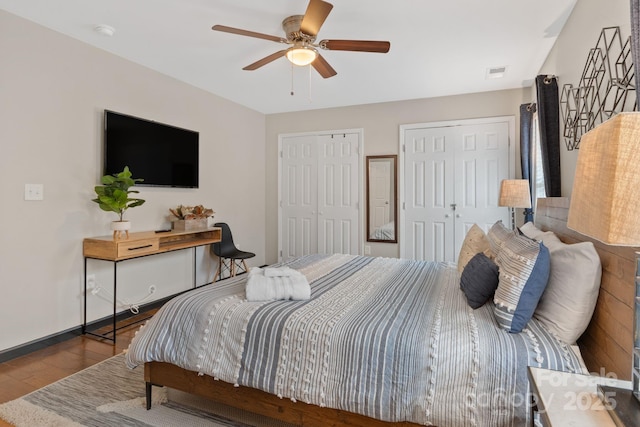 bedroom featuring baseboards, visible vents, ceiling fan, wood finished floors, and two closets