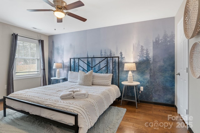 bedroom with a ceiling fan, visible vents, baseboards, and wood finished floors