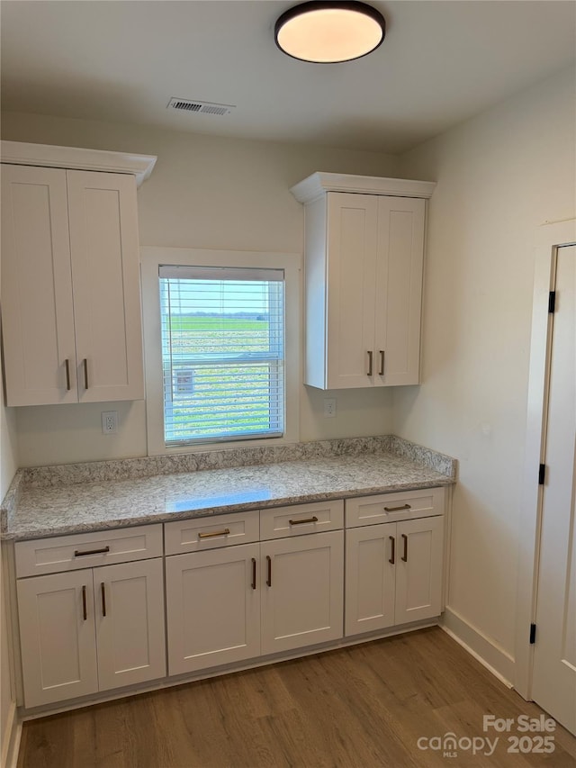 kitchen with visible vents, white cabinets, light wood-style flooring, and baseboards