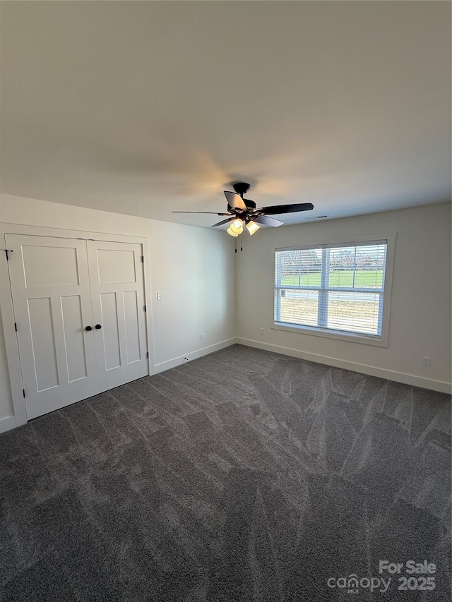 unfurnished room with baseboards, dark carpet, and ceiling fan