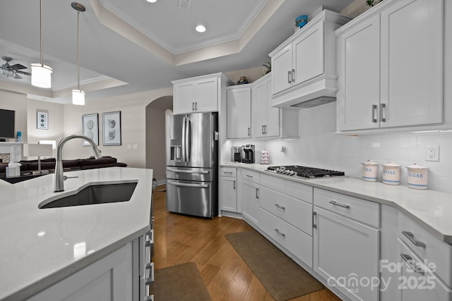 kitchen featuring a tray ceiling, arched walkways, dark wood finished floors, appliances with stainless steel finishes, and a sink