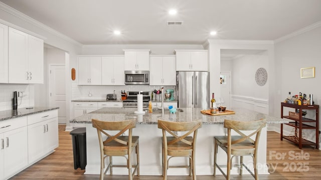 kitchen with a breakfast bar area, light wood-style flooring, visible vents, appliances with stainless steel finishes, and an island with sink