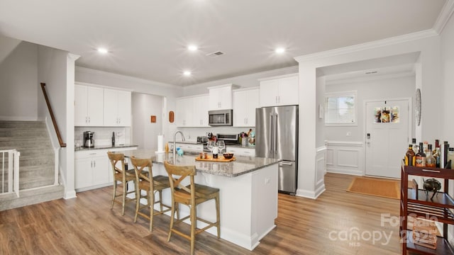 kitchen with an island with sink, appliances with stainless steel finishes, light wood-style floors, a kitchen bar, and a sink