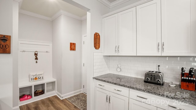 kitchen featuring dark wood-style flooring, crown molding, tasteful backsplash, white cabinetry, and dark stone counters