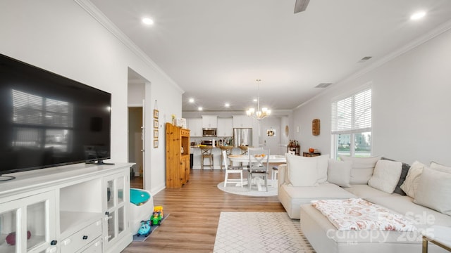 living room featuring a notable chandelier, crown molding, visible vents, and light wood finished floors