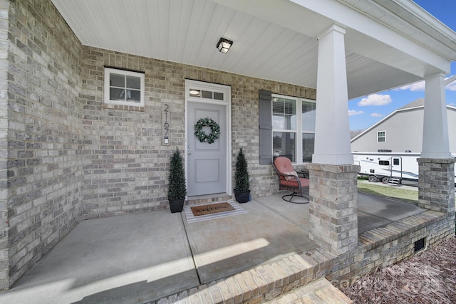 entrance to property featuring a porch and brick siding