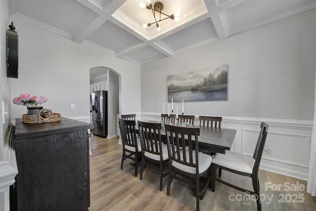 dining room featuring light wood finished floors, arched walkways, and beam ceiling