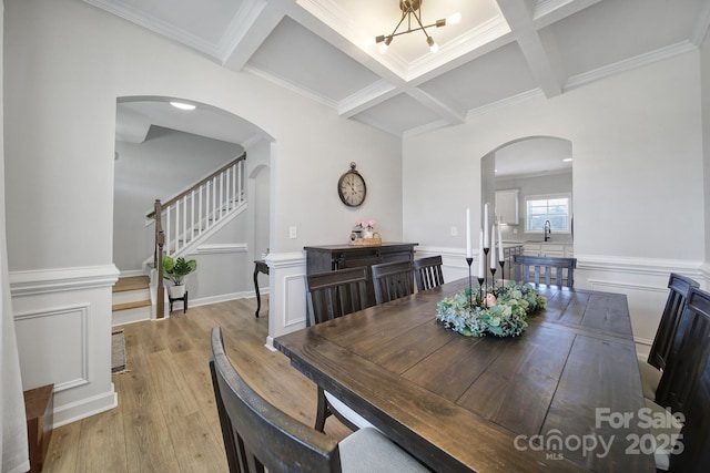 dining space with arched walkways, coffered ceiling, beamed ceiling, and light wood finished floors