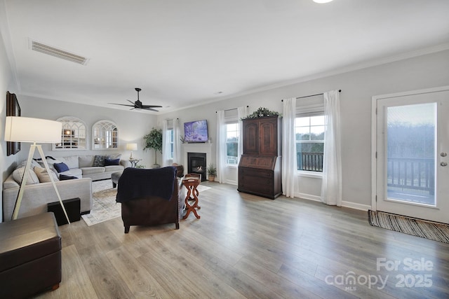 living room featuring ornamental molding, a glass covered fireplace, wood finished floors, and visible vents