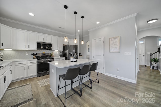 kitchen with arched walkways, a kitchen island, appliances with stainless steel finishes, a breakfast bar, and white cabinetry