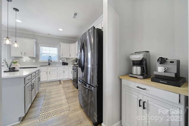 kitchen featuring visible vents, freestanding refrigerator, a sink, light countertops, and backsplash