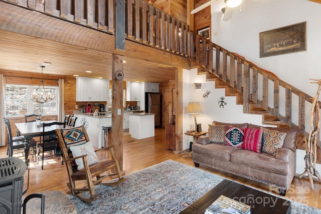 living area with light wood-style flooring, ceiling fan with notable chandelier, stairs, and a high ceiling