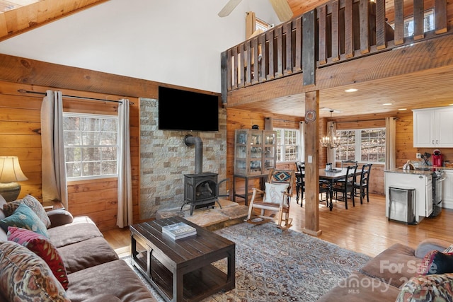 living area featuring wooden walls, light wood-style flooring, a wood stove, and high vaulted ceiling