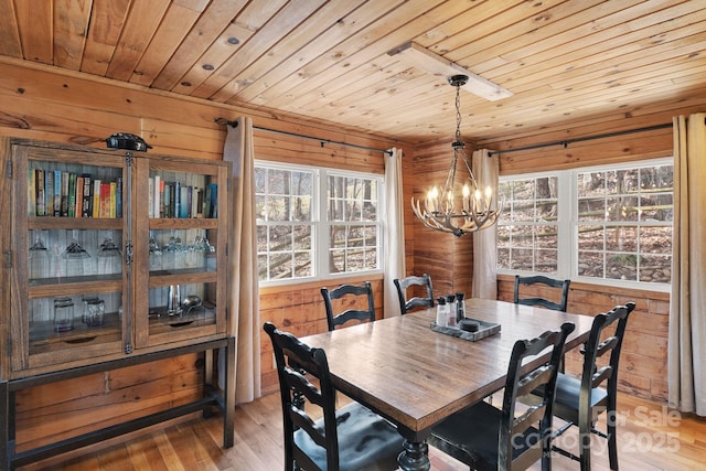 dining room featuring wooden walls, wood ceiling, light wood-type flooring, and an inviting chandelier