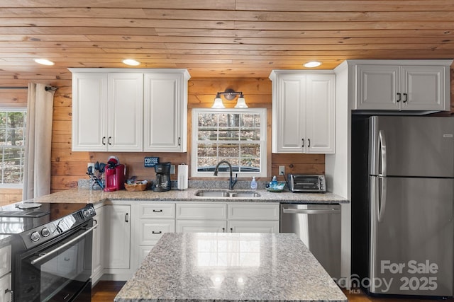 kitchen with wood walls, appliances with stainless steel finishes, wooden ceiling, white cabinets, and a sink