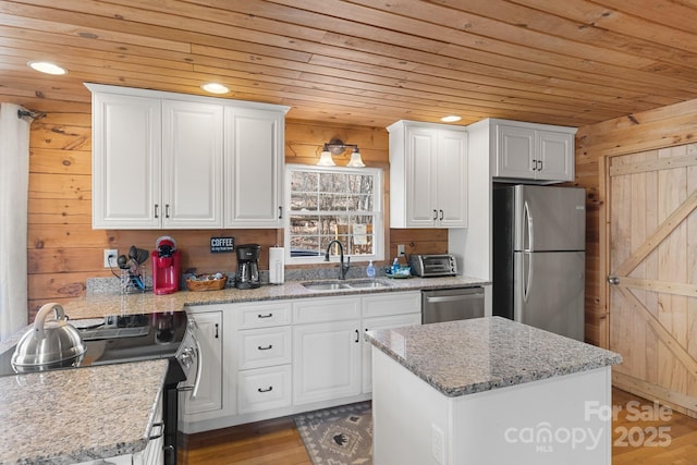 kitchen featuring wood walls, wood ceiling, white cabinets, stainless steel appliances, and a sink