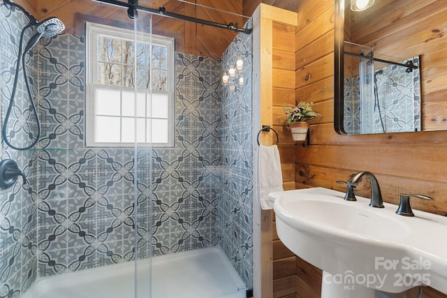 bathroom with a sink, wood walls, and tiled shower