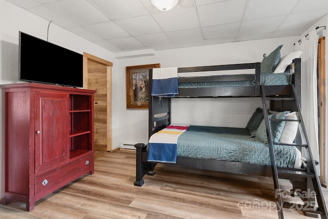 unfurnished bedroom featuring baseboard heating, light wood-style flooring, and a paneled ceiling