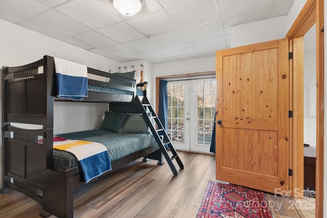 bedroom with a drop ceiling, access to outside, wood finished floors, and french doors