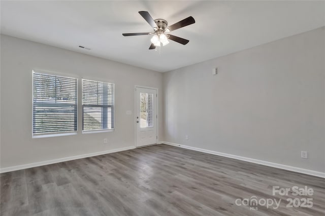 empty room with dark wood-style floors, a ceiling fan, visible vents, and baseboards