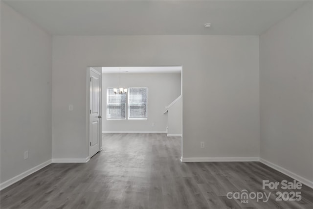 unfurnished room featuring a notable chandelier, baseboards, and wood finished floors