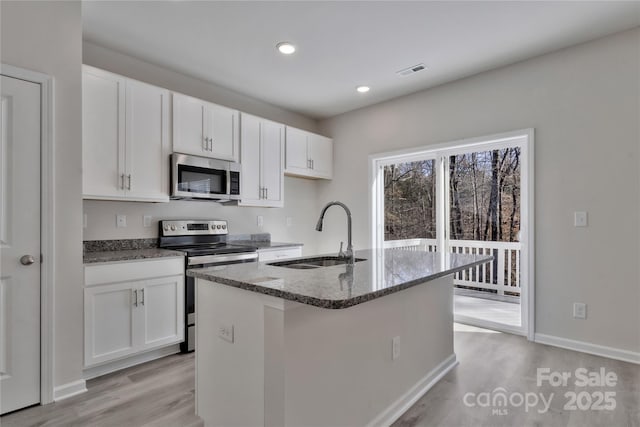 kitchen with stainless steel appliances, visible vents, a sink, an island with sink, and dark stone counters