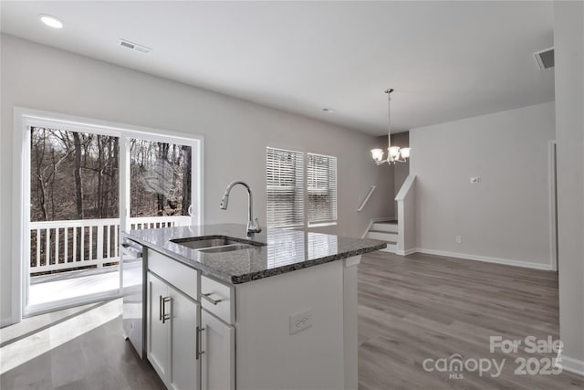 kitchen featuring wood finished floors, dark stone countertops, a sink, and visible vents