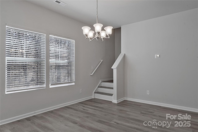 unfurnished dining area with a notable chandelier, wood finished floors, visible vents, baseboards, and stairs