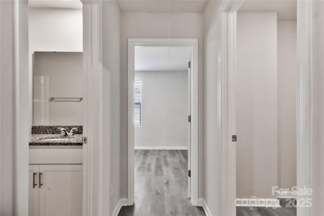 corridor featuring attic access, baseboards, a sink, and wood finished floors