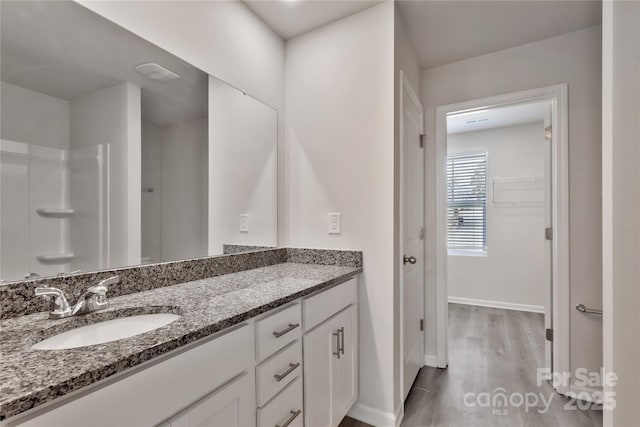 bathroom featuring walk in shower, wood finished floors, vanity, and baseboards