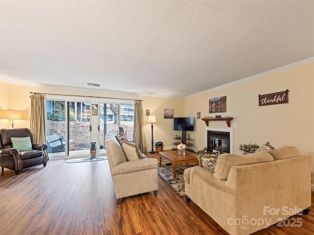 living area with dark wood-style floors, a glass covered fireplace, visible vents, and ornamental molding