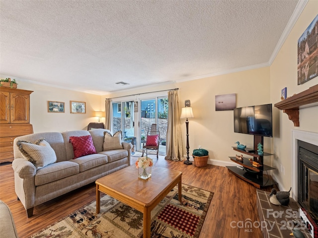 living room with wood finished floors, visible vents, baseboards, a glass covered fireplace, and crown molding