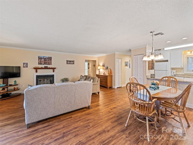 dining area featuring dark wood-type flooring, a glass covered fireplace, crown molding, and a textured ceiling